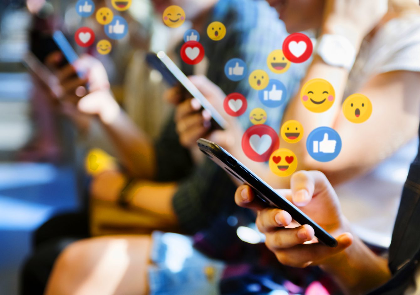 Row of people using smartphones with social media reaction emojis around