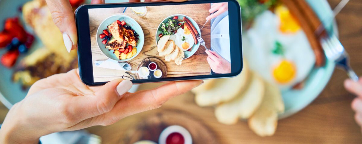 Hands holding smartphone taking photo of restaurant food