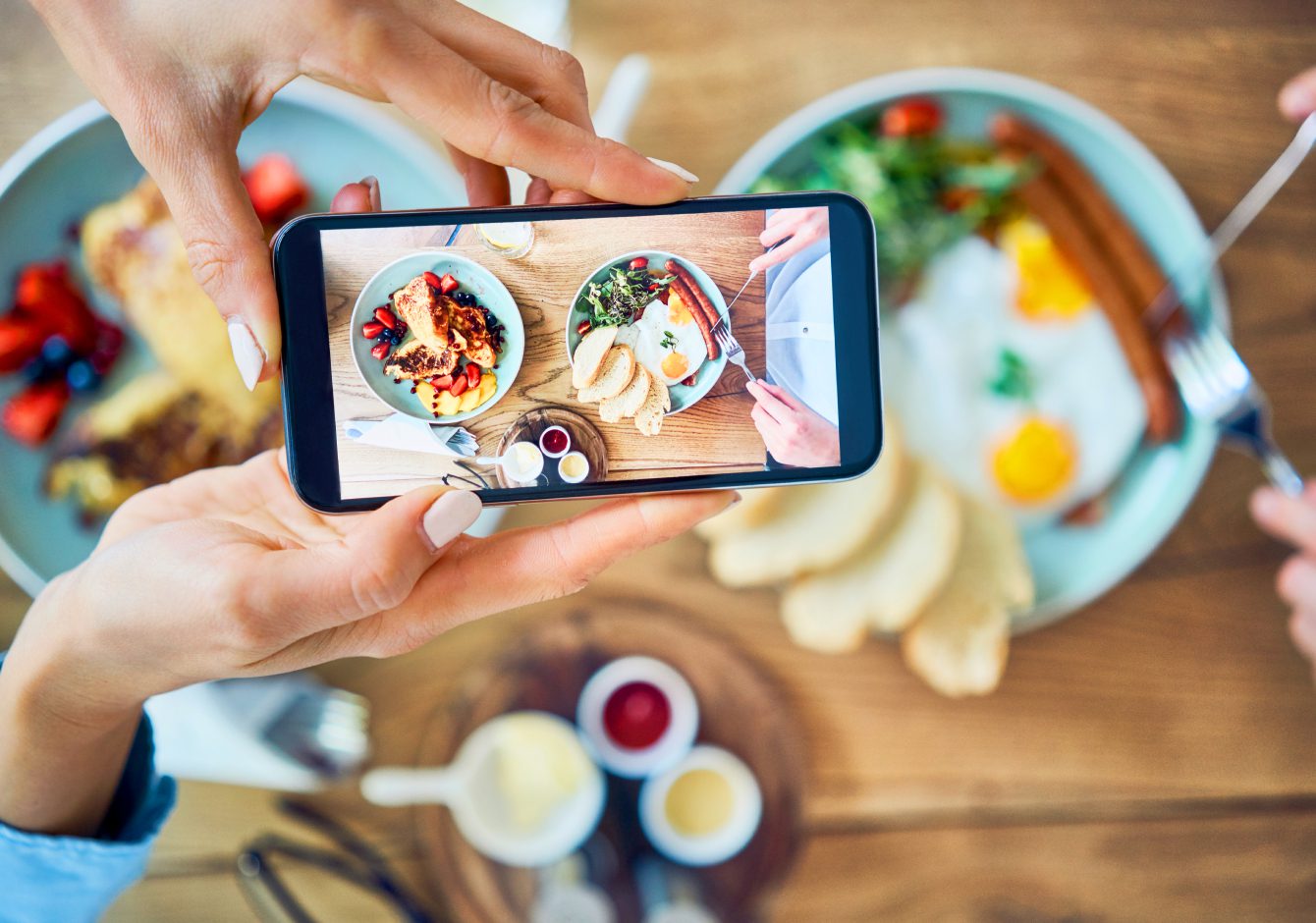 Hands holding smartphone taking photo of restaurant food