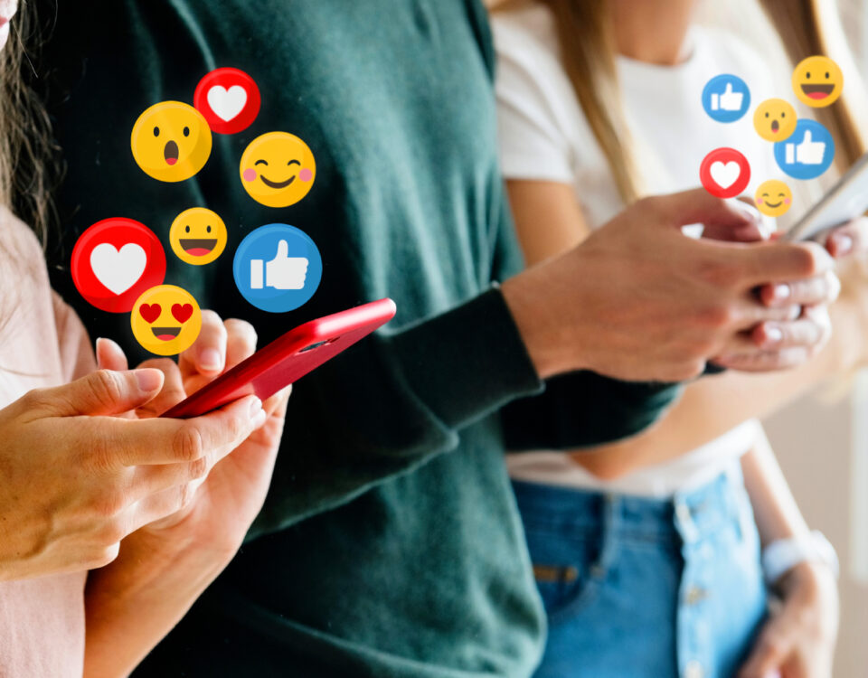 Row of people holding smartphones with social media reaction emojis around the screens