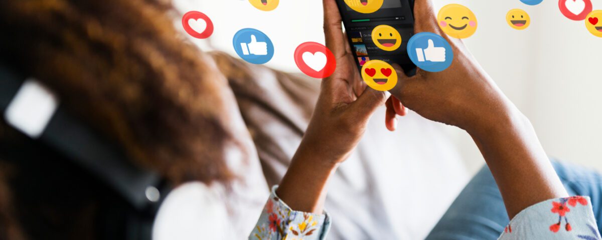 Woman lounging on sofa using smartphone with social media reaction emojis around