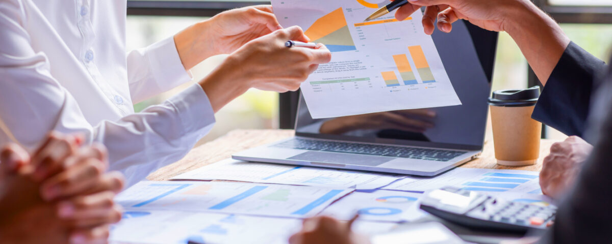 Office team members sitting at desk pointing to data graphs on a sheet of paper