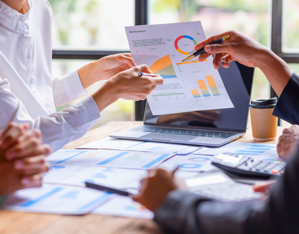 Office team members sitting at desk pointing to data graphs on a sheet of paper