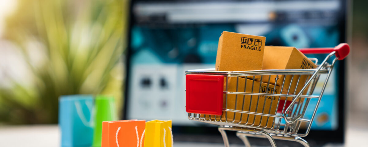 Laptop on desk with miniature shopping cart and shopping bags in front of it