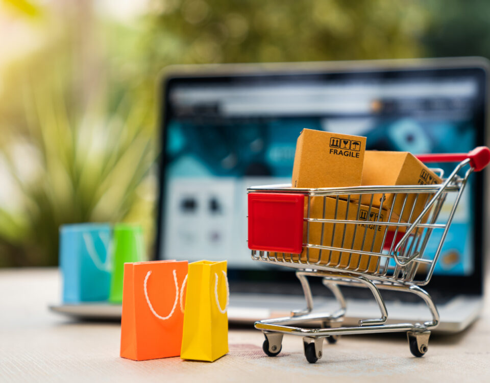 Laptop on desk with miniature shopping cart and shopping bags in front of it