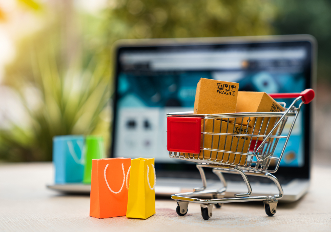 Laptop on desk with miniature shopping cart and shopping bags in front of it