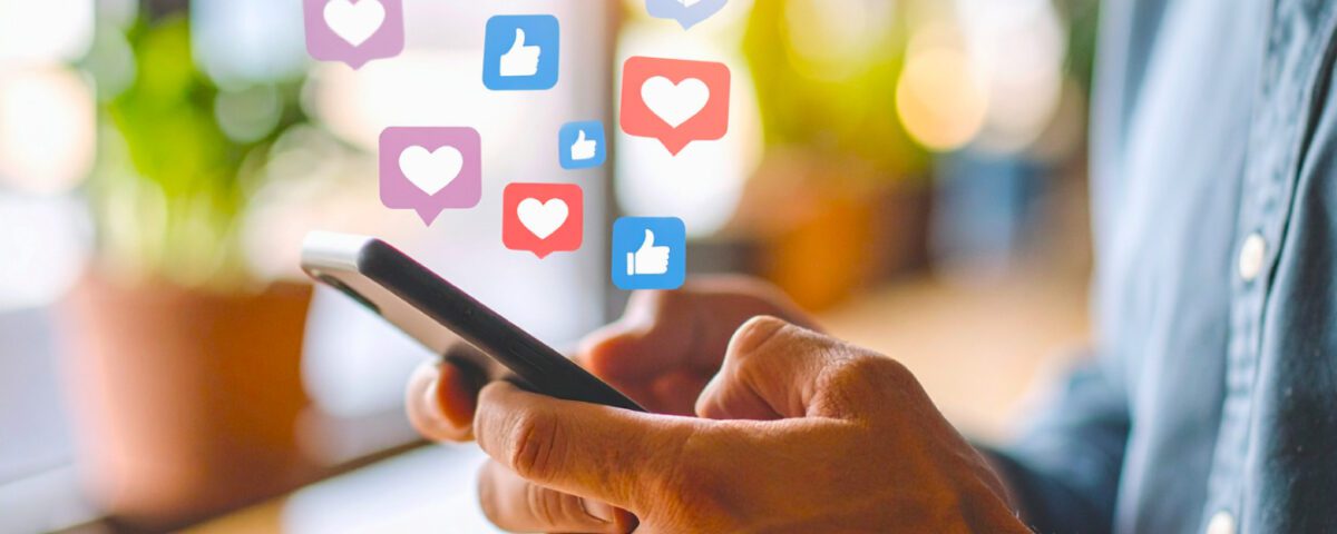 Man holding smartphone with social media reaction emojis around