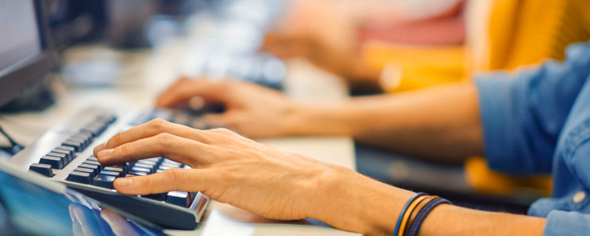 Row of people sitting at desk in office typing on computer keyboards