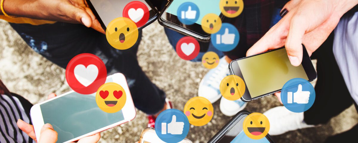 Group of people standing in a circle using smartphones with social media reaction emojis coming from the screens