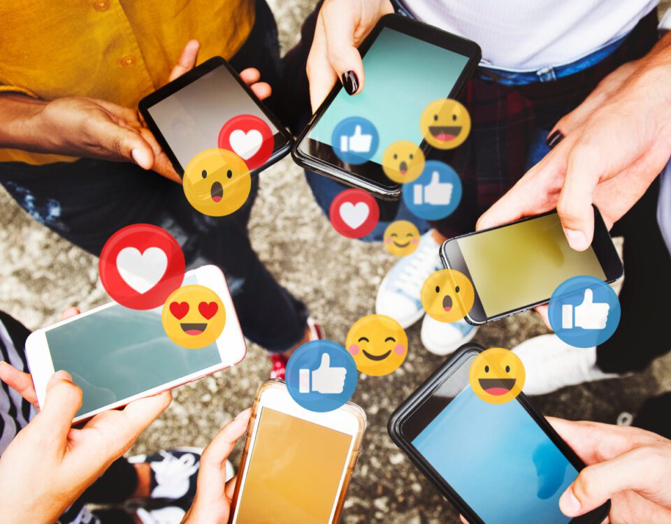 Group of people standing in a circle using smartphones with social media reaction emojis coming from the screens