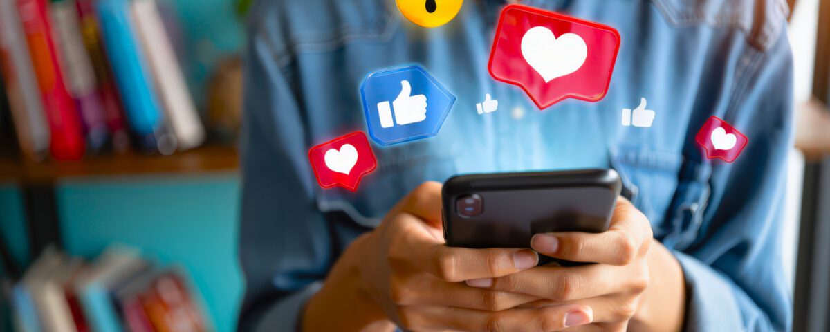 Woman in blue shirt holding smartphone with social media reaction emojis around