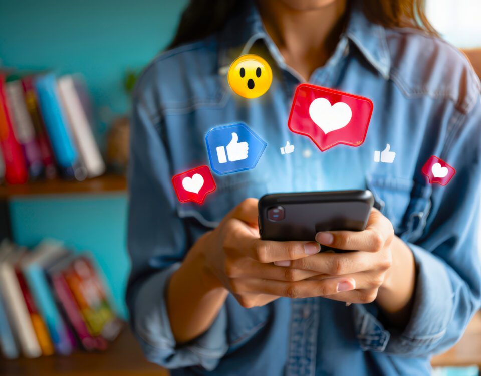 Woman in blue shirt holding smartphone with social media reaction emojis around